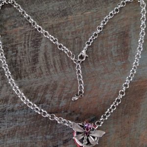Silver chain necklace with a dragonfly-shaped pendant adorned with red stones laid on a wooden surface, showing the clasp.